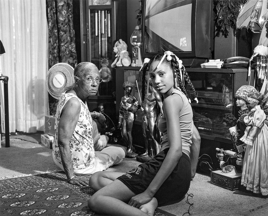 Schwarzweißfoto einer älteren Frau und einer jüngeren Frau, die vor der Kamera auf dem Boden des Wohnzimmers sitzen