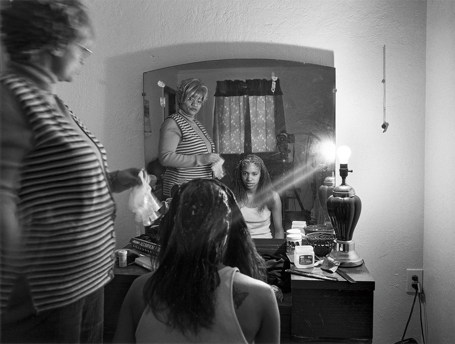 Schwarzweißfoto einer stehenden Frau mit einem sitzenden Mädchen, die beide in den Spiegel schauen