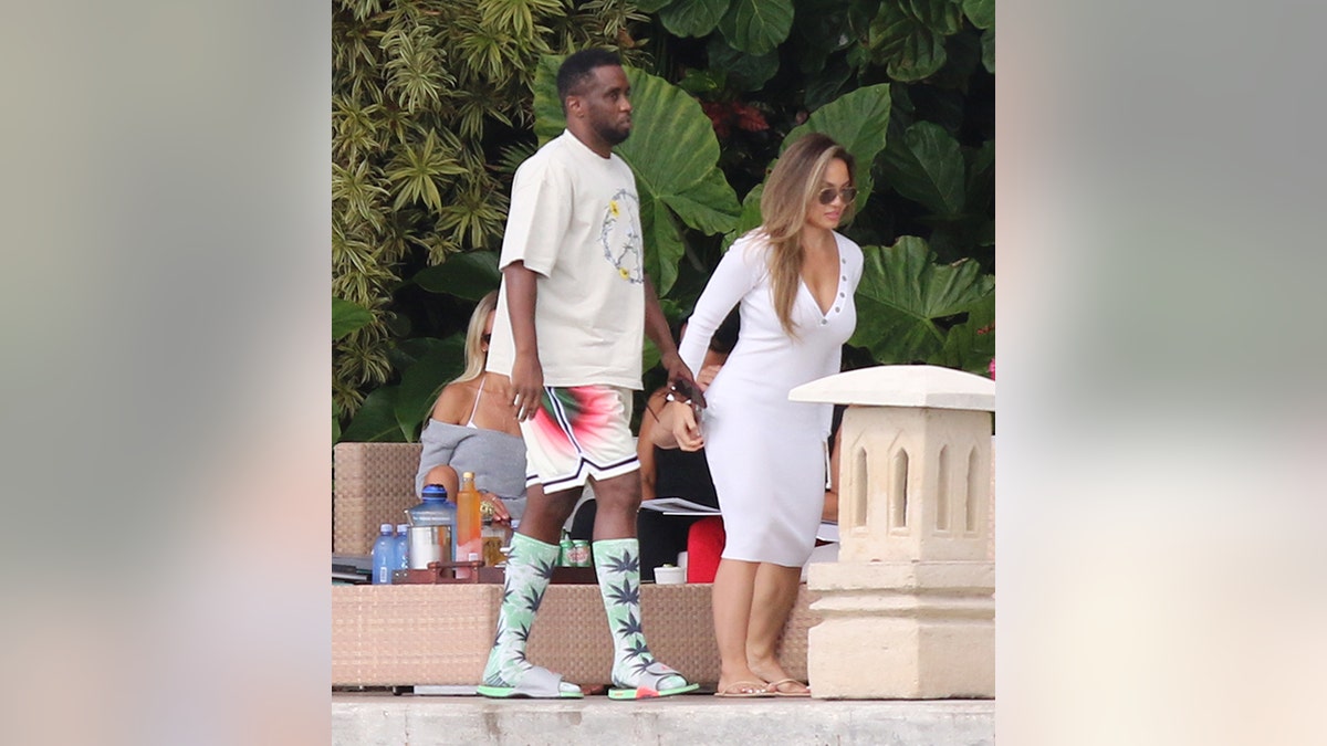 Diddy in einem weißen Hemd und weißen, roten und grünen Shorts läuft neben Daphne Joy in einem weißen Kleid in Miami Beach