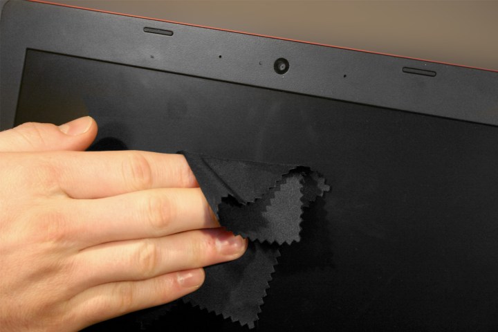 Die Hand einer Person reinigt den Bildschirm eines Laptops mit einem Mikrofasertuch.