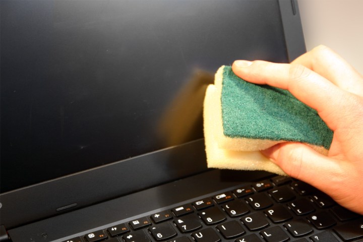 Die Hand einer Person reinigt den Bildschirm eines Laptops mit einem Schwamm.