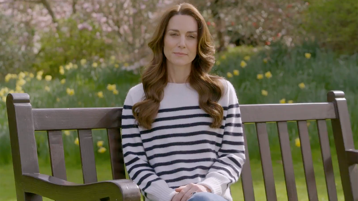 Kate Middleton sitzt in einem weißen Top mit marineblauen Streifen auf einer Bank und verkündet, dass sie Krebs hat