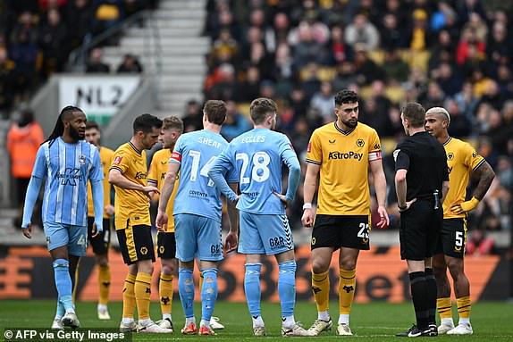 Referee English referee Samuel Barrott waits with players while a VAR (Video Assistant Referee) review is carried out following a 'goal' by Coventry City's English striker #09 Ellis Simms during the English FA Cup Quarter-final football match between Wolverhampton Wanderers and Coventry City at the Molineux stadium in Wolverhampton, central England on March 16, 2024. (Photo by Paul ELLIS / AFP) / RESTRICTED TO EDITORIAL USE. No use with unauthorized audio, video, data, fixture lists, club/league logos or 'live' services. Online in-match use limited to 120 images. An additional 40 images may be used in extra time. No video emulation. Social media in-match use limited to 120 images. An additional 40 images may be used in extra time. No use in betting publications, games or single club/league/player publications. /  (Photo by PAUL ELLIS/AFP via Getty Images)
