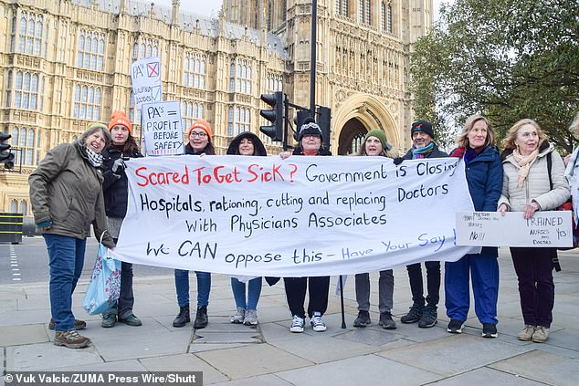 Die Mail on Sunday hat nun herausgefunden, dass der NHS „Lehrstellen“ für PAs einführt.  Demonstranten halten ein Banner vor dem Parlamentsgebäude