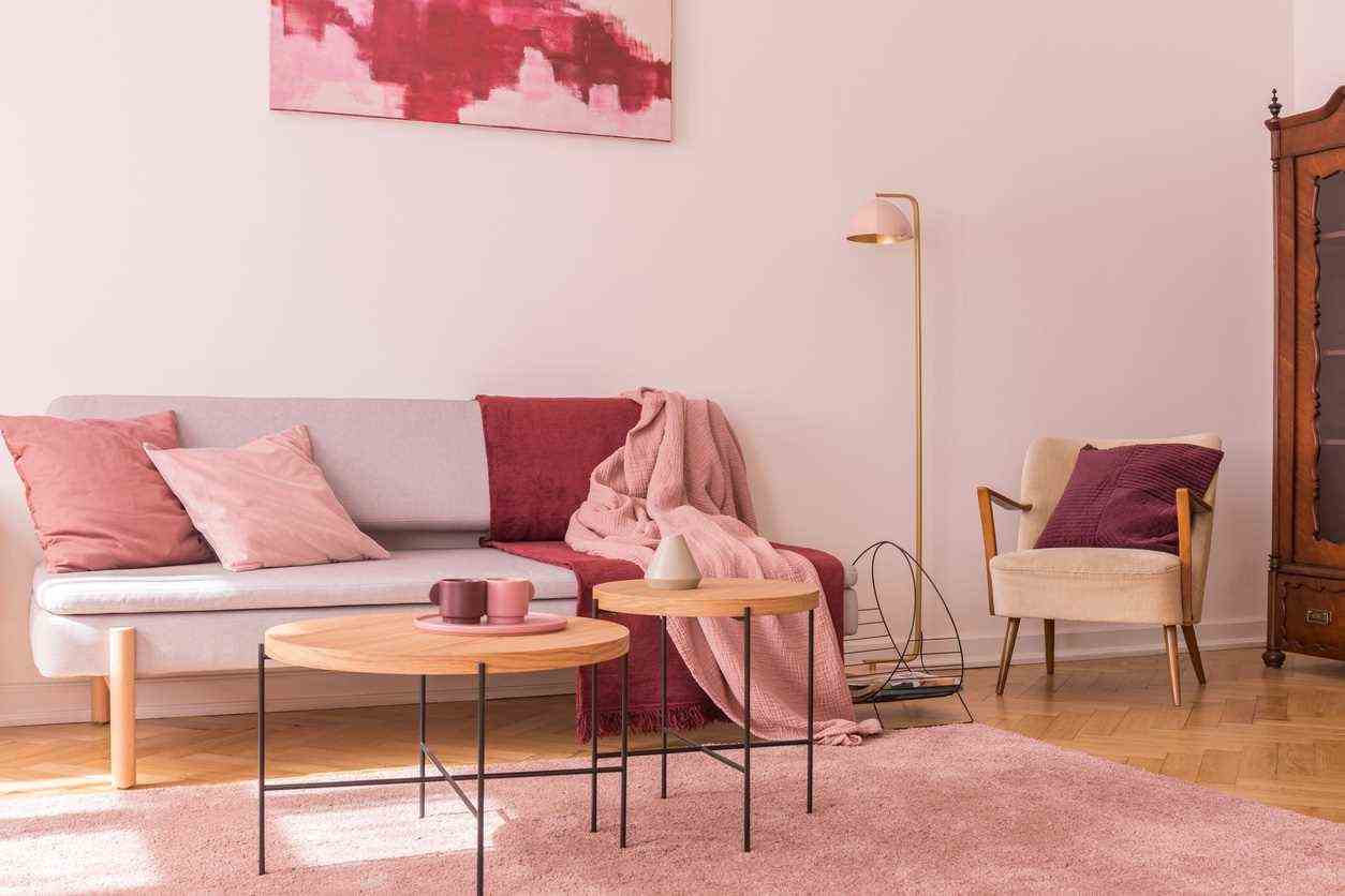 Two Wooden Coffee Tables Next To Modern Gray Sofa With Pillows And Blankets In Lovely Pastel Pink Living Room Interior