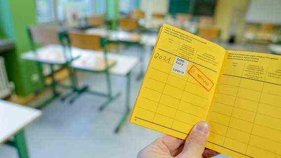 A vaccination card is held up in a classroom.  © picture alliance / Flashpic Photo: Jens Krick