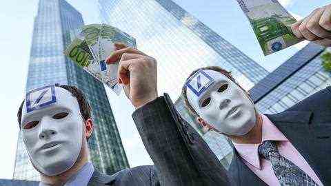 Two men with masks hold up bills in front of the Deutsche Bank.