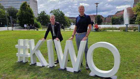 Kiel's Mayor Ulf Kämper (SPD) and regatta director Dirk Ramhorst stand on a meadow in front of white letters "#KIWO".  © NDR Photo: Kai Peuckert