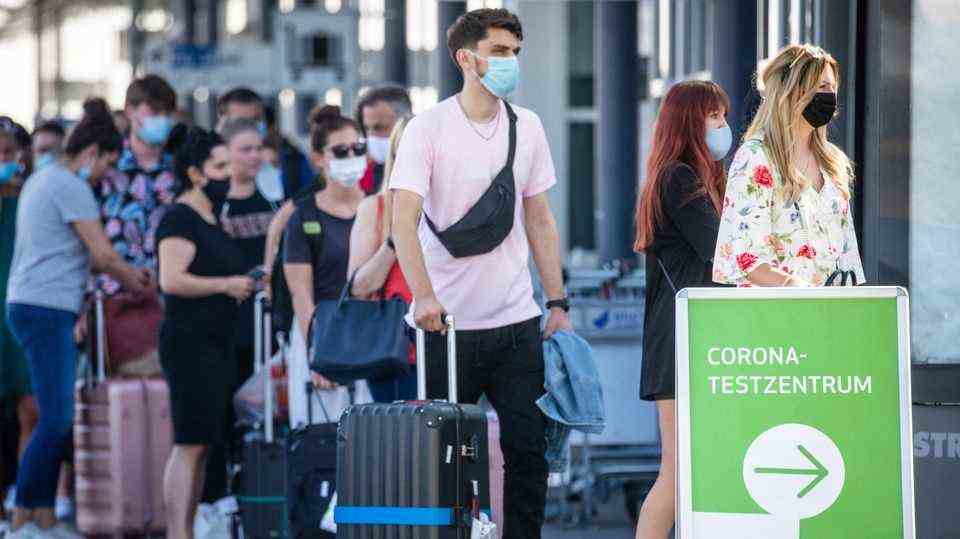 Reiserückkehrer aus Spanien stehen mit Mundschutz vor dem Corona-Testzentrum am Flughafen Stuttgart an