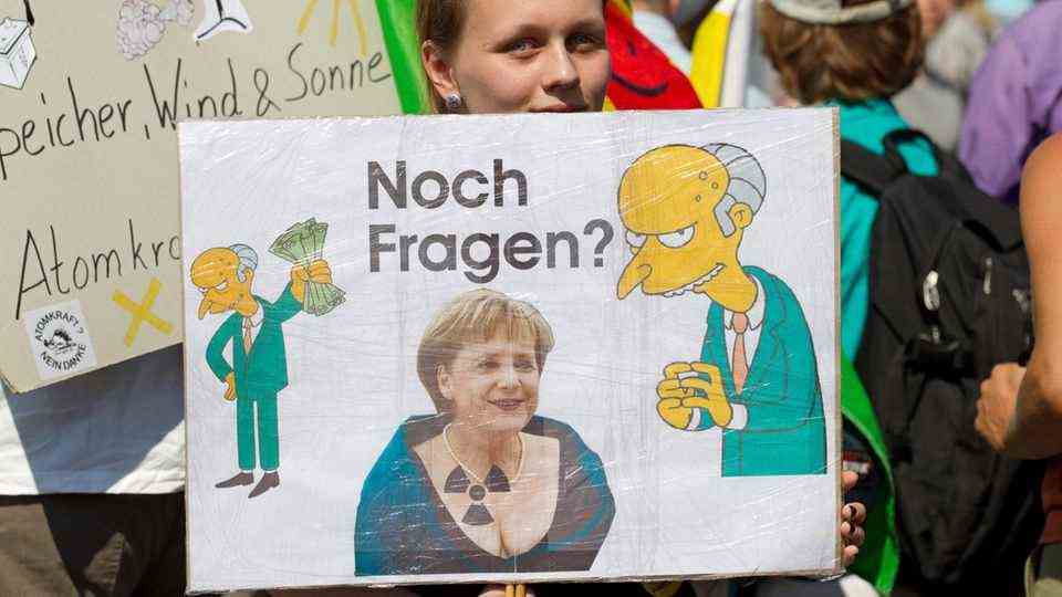 A demonstrator in Gronau holds a banner against nuclear power with Merkel and Mister Burns on it in her hand.