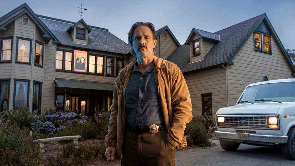 Sheriff Dewey "Dwight" Riley stands in front of the Scream House