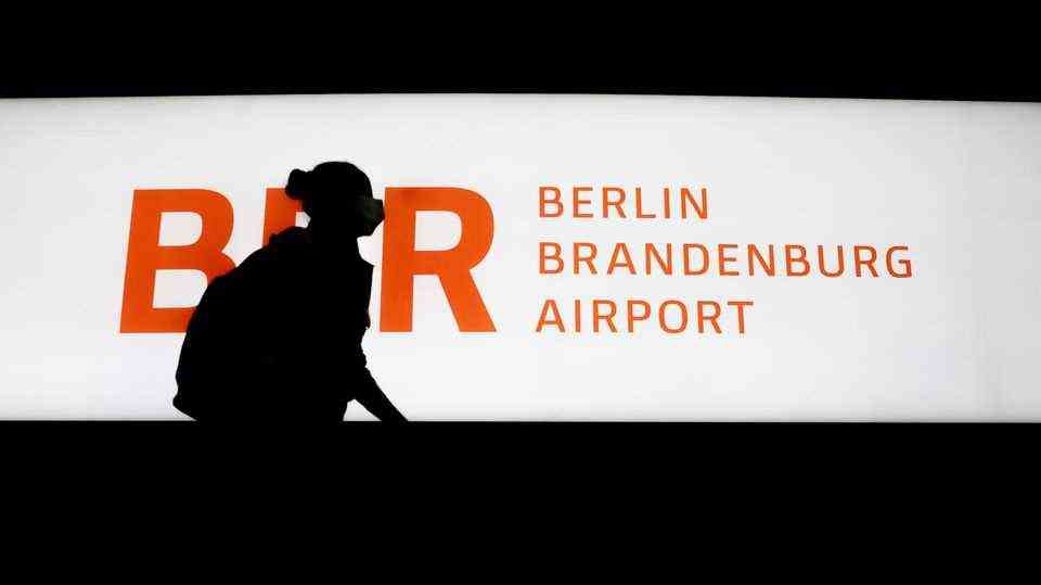 Passenger walks past an illuminated sign BER Berlin Brandenburg Airport