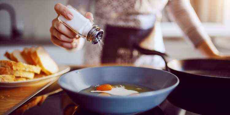 A woman is salting fried eggs in a pan