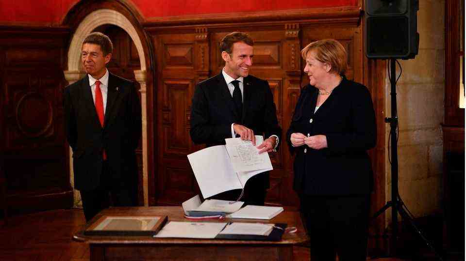 Merkel is congratulated by Emmanuel Macron (M) after being awarded the Grand Cross of the Legion of Honor, Joachim Sauer on the left