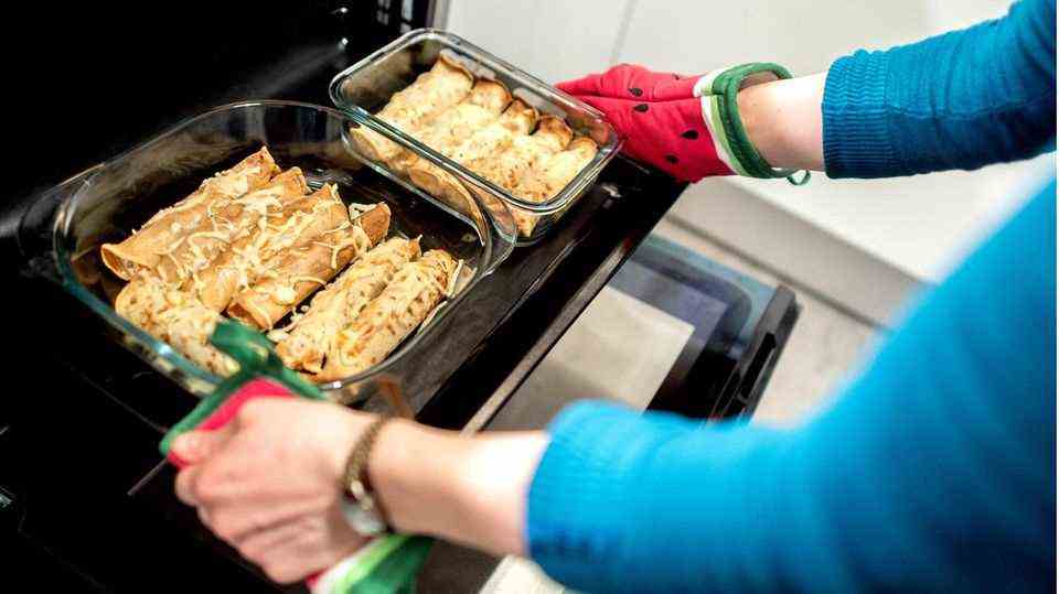 A woman in a blue sweater uses red and green pot holders to get a baking sheet with rolling pin from an oven