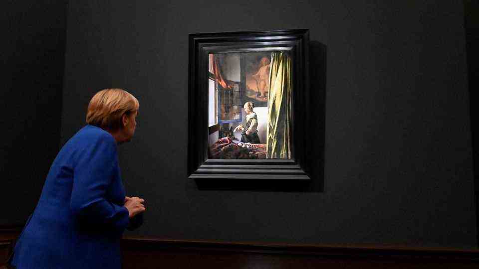 Chancellor Merkel bends over to a painting and examines it closely
