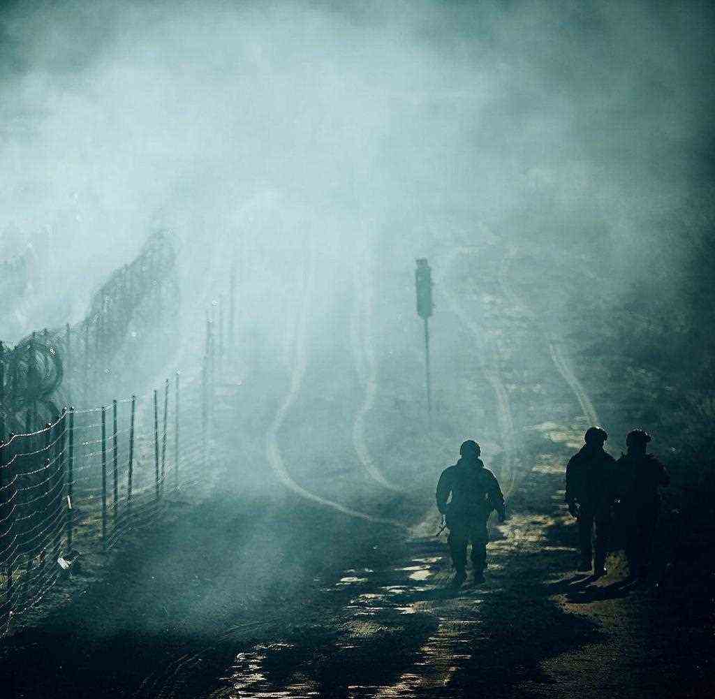 ARCHIVE - 11/12/2021, Poland, Kuznica: Polish security forces walk along a barbed wire fence at the Polish-Belarusian border crossing in Kuznica in the dark, while smoke from campfires settles over a migrant camp.  According to the Defense Ministry, Polish security forces stopped a group of migrants at the Polish-Belarusian border crossing in Kuznica.  The group then began to march along the border barrier.  Photo: Irek Doro¿añski / Dwot / DWOT / dpa +++ dpa-Bildfunk +++