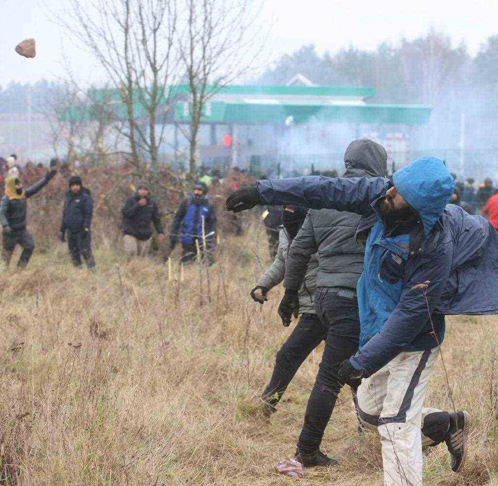 A man throws a stone towards the Polish border fence and Polish security forces on Tuesday as migrants tried to enter Poland