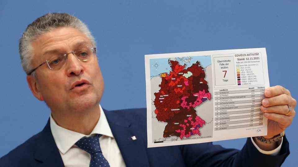 Eoin, a white man with white-gray curly hair, holds up with his left a map of Germany with counties colored in different colors