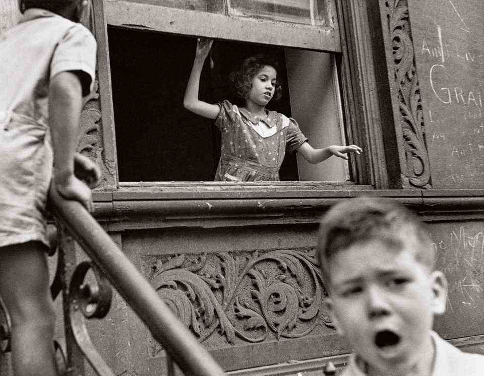 A girl is chatting with children in the street from the window of her apartment