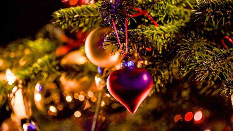 Bei gedämpftem Licht hängen eine goldene Kugel und ein rotes Herz als Schmuck an einem Weihnachtsbaum