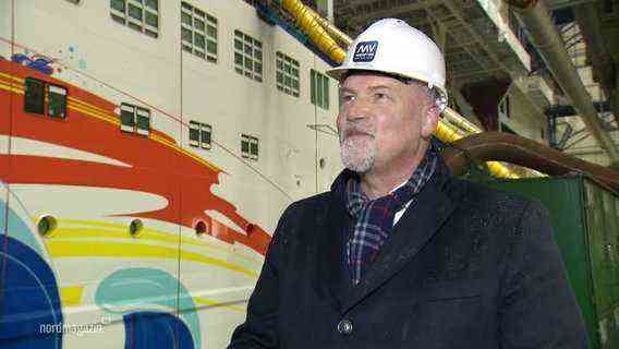 Carsten Haake, Managing Director of MV Werften, stands in front of a cruise ship that is being built in a hall.  © screenshot 