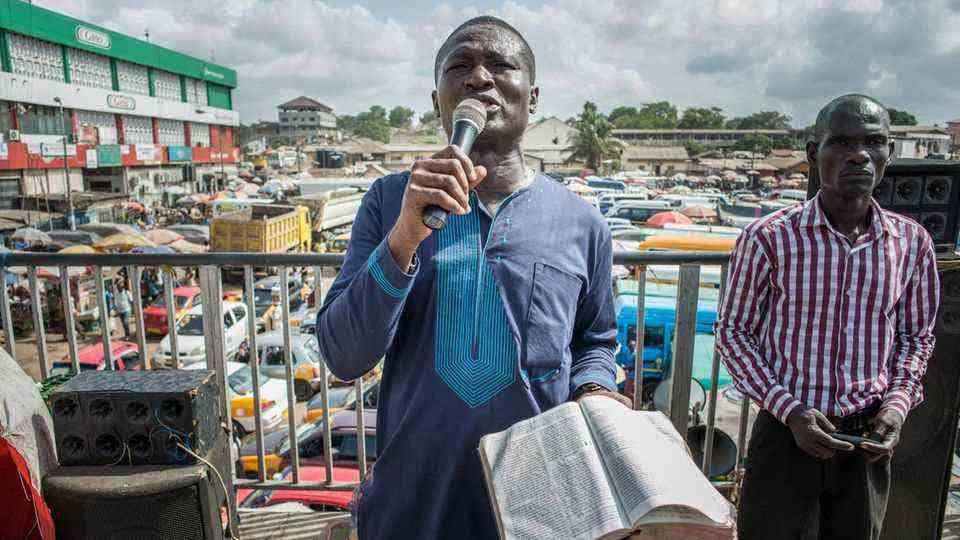 A man stands with a microphone in his right hand and a Bible in his left in Accra's main market square.