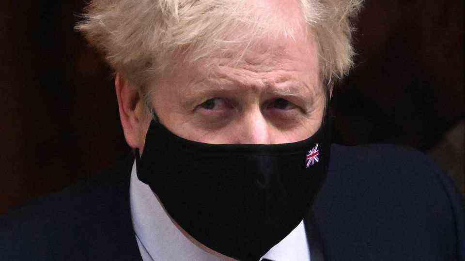 A white man with messy white-blonde hair and a black mask with a Union Jack leaves a house in a suit and tie