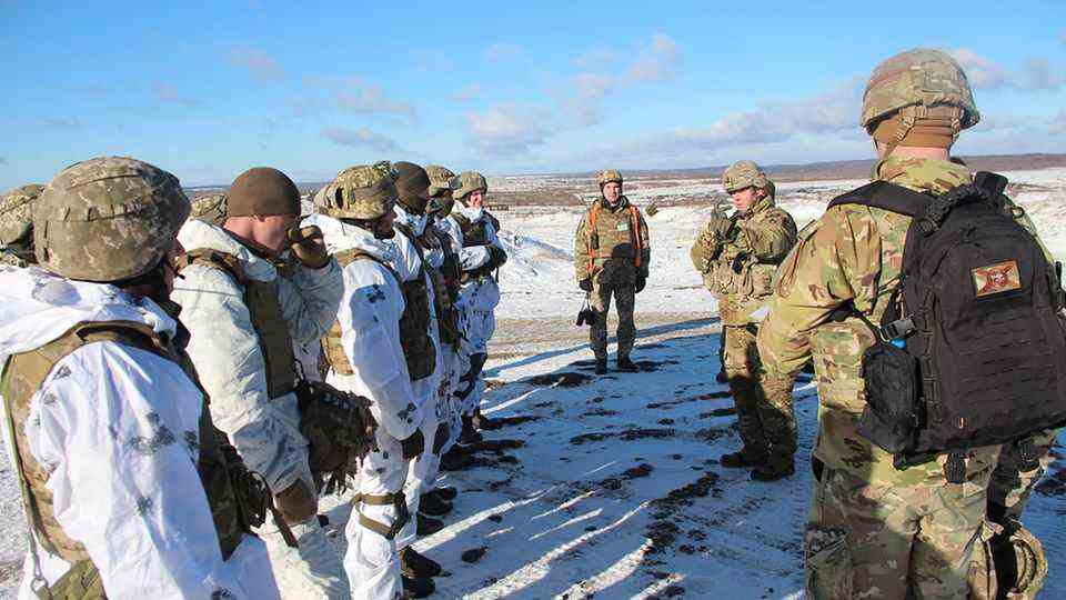 On the left is a line of US soldiers in white overalls, in front of them are three from Ukraine in camouflage