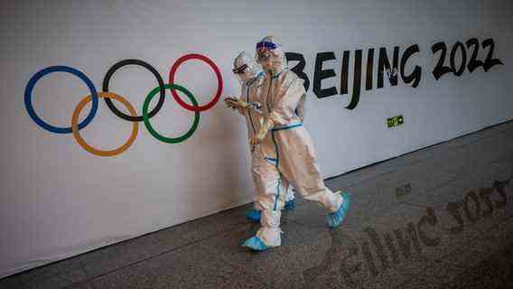 Helpers in full protective gear go to the Olympic rings and the lettering "Beijing 2022" past.  © picture alliance/dpa Photo: Michael Kappeler