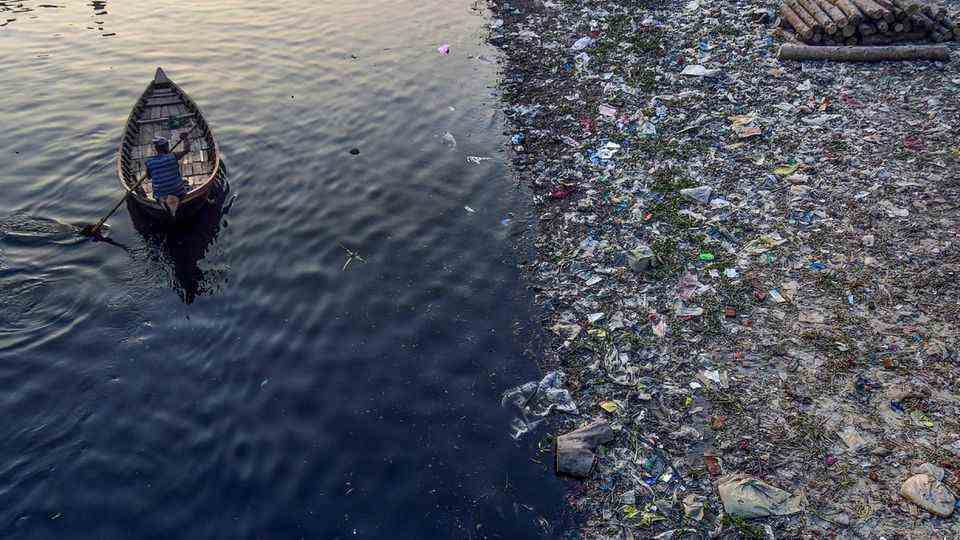 A man rows past plastic waste in Dhaka, Bangladesh