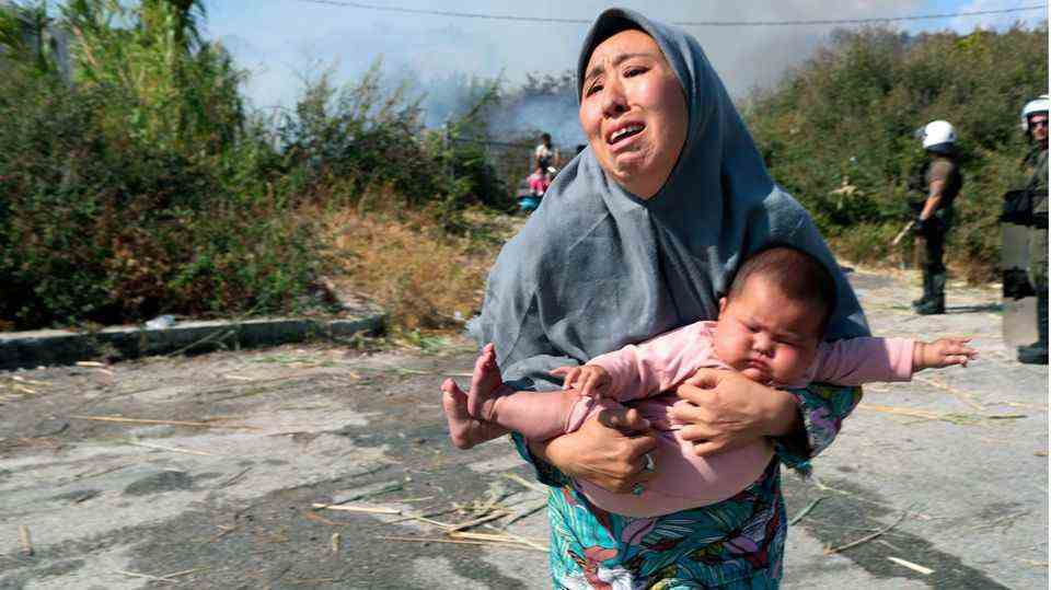 Woman holds her baby while escaping a small fire in a field near the city of Mytilene