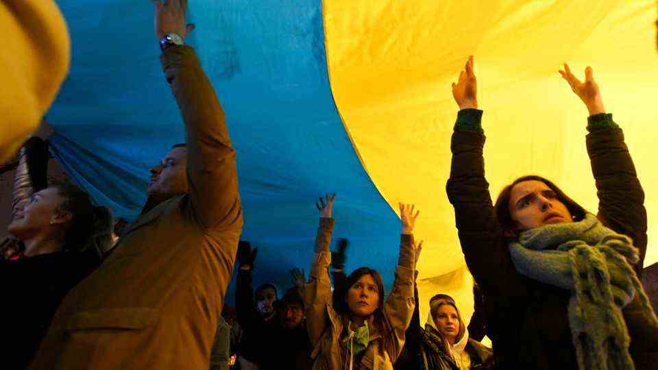 People take part in a demonstration in front of the Russian embassy with a huge Ukrainian flag