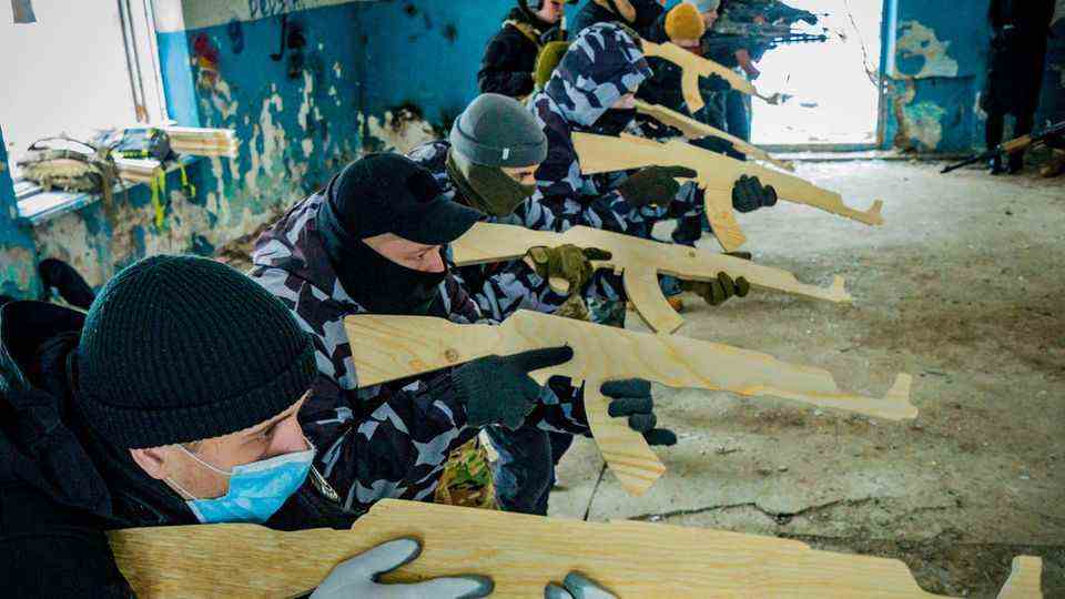 Volunteers learn how to aim a wooden practice rifle at a military exercise indoors