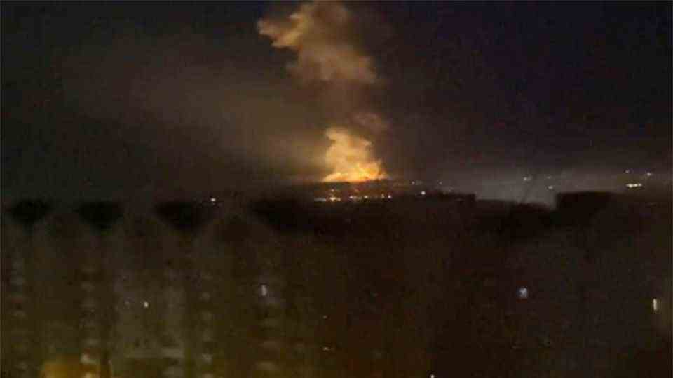 A pixelated photo shows firelight and smoke behind a long block of flats