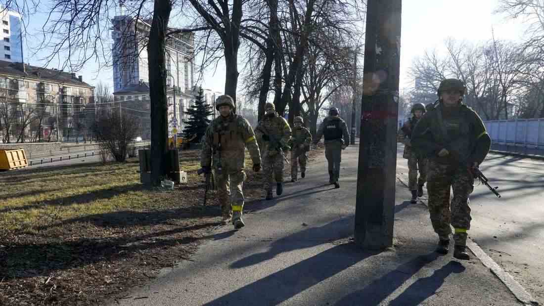 Ukrainische Soldaten patrouillieren, nicht weit von brennenden Militärfahrzeugen entfernt. Russische Truppen haben den erwarteten Angriff auf die Ukraine gestartet und drangen in die Hauptstadt vor.