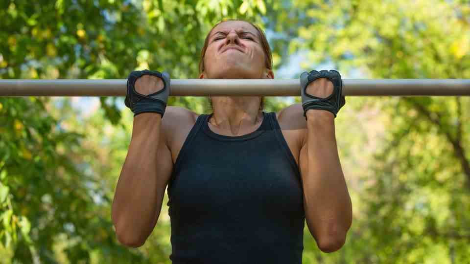 A woman with a strained face tries a pull-up
