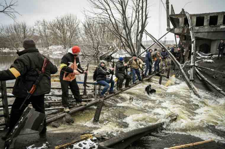 Members of the Ukrainian civil defense cross a river whose bridge was destroyed, north of Kiev, on March 1, 2022 ( AFP / ARIS MESSINIS )