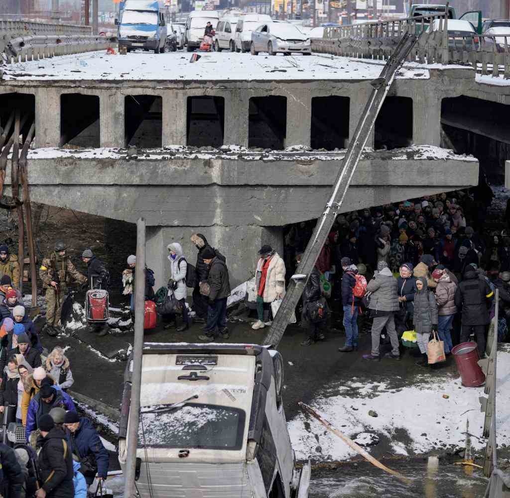 Ukrainische Männer und Frauen stehen auf der Flucht aus Irpin vor einer zerstörten Brücke