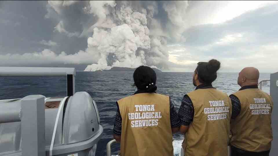 Three people watch the volcanic eruption from afar
