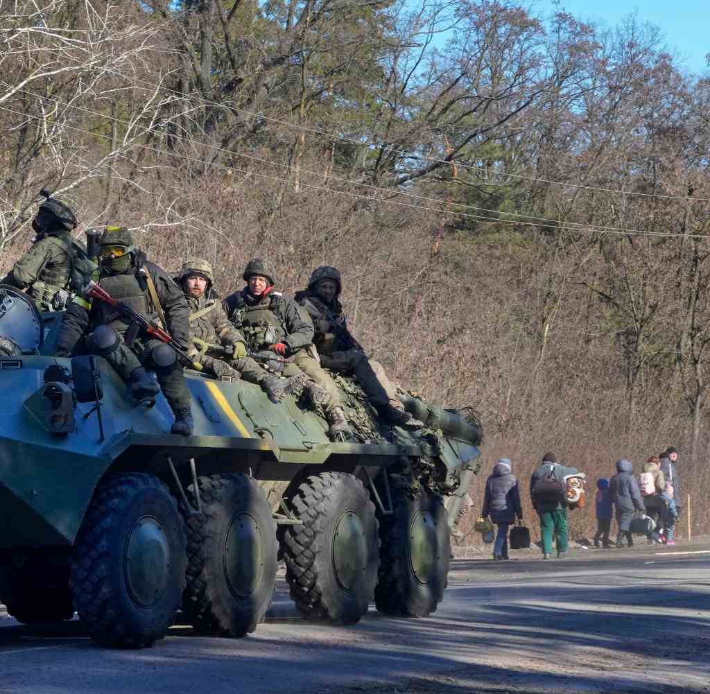 Ukrainische Soldaten auf einem Panzer in der Nähe von Kiew - im Hintergrund fliehende Zivilisten