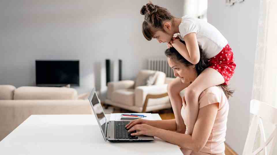 Mother with a child on her shoulders sits in front of the computer
