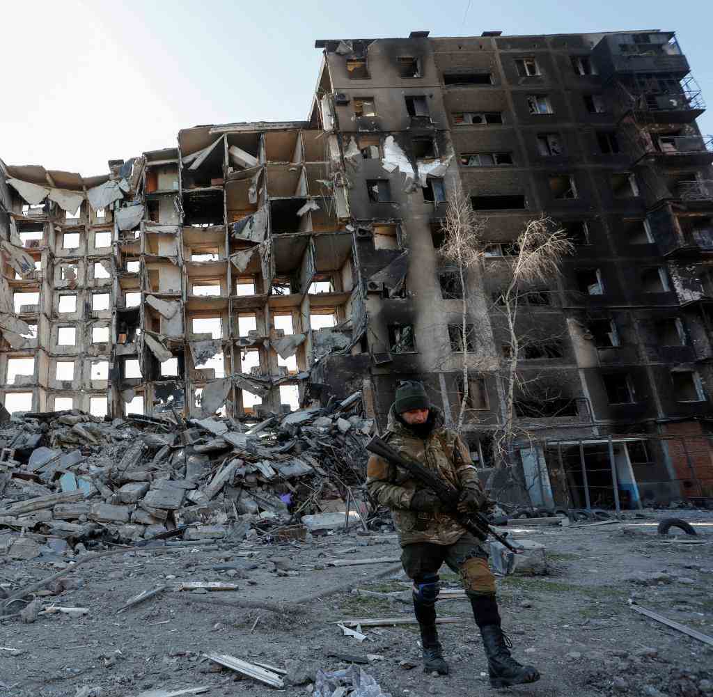 A soldier from Russian units in front of a destroyed building in Mariupol