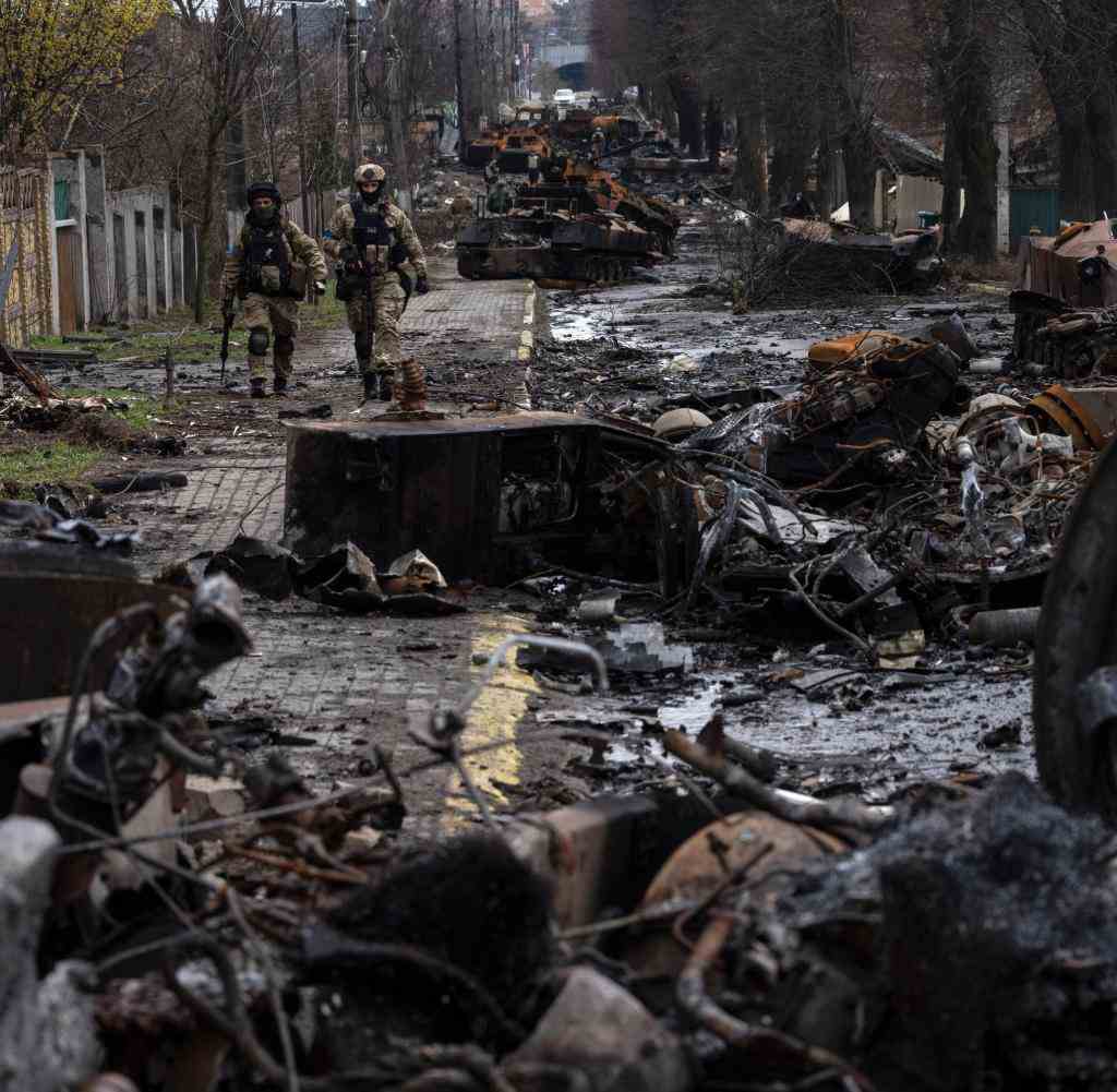 Two Ukrainian soldiers walk on a street in the city of Bucha, which is littered with wrecked Russian military vehicles