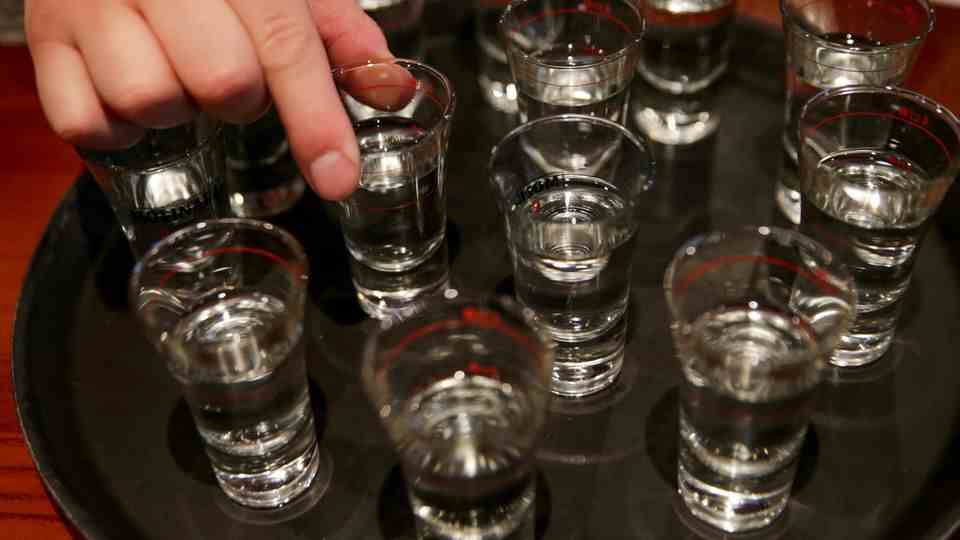 Shot glasses with clear liquid stand on a round black tray.  A hand lifts one of the glasses.
