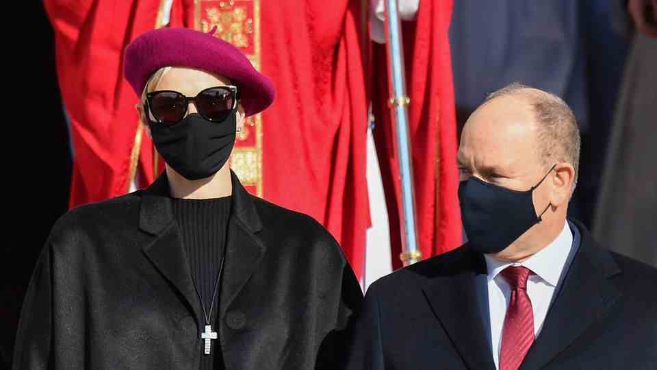 An elegantly dressed woman with a burgundy beret, sunglasses and a black face mask is standing next to a smaller man