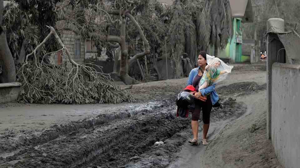 The Taal volcano in the Philippines has veiled the landscape and people are fleeing.  A woman carries a statue of the baby Jesus to safety in the town of Boso-Boso.