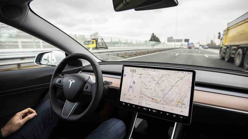 A man is behind the wheel of a Tesla car and does not have his hands on the wheel while driving.