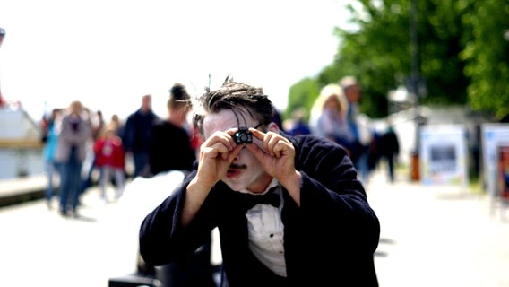 A street performer is holding a tiny camera.  © NDR Photo: Lisa Pandelaki