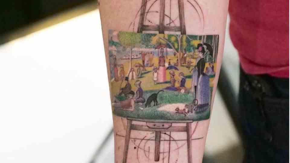 A painting on an easel shows people in the park.  It stands on an easel and is a tattoo on one arm.